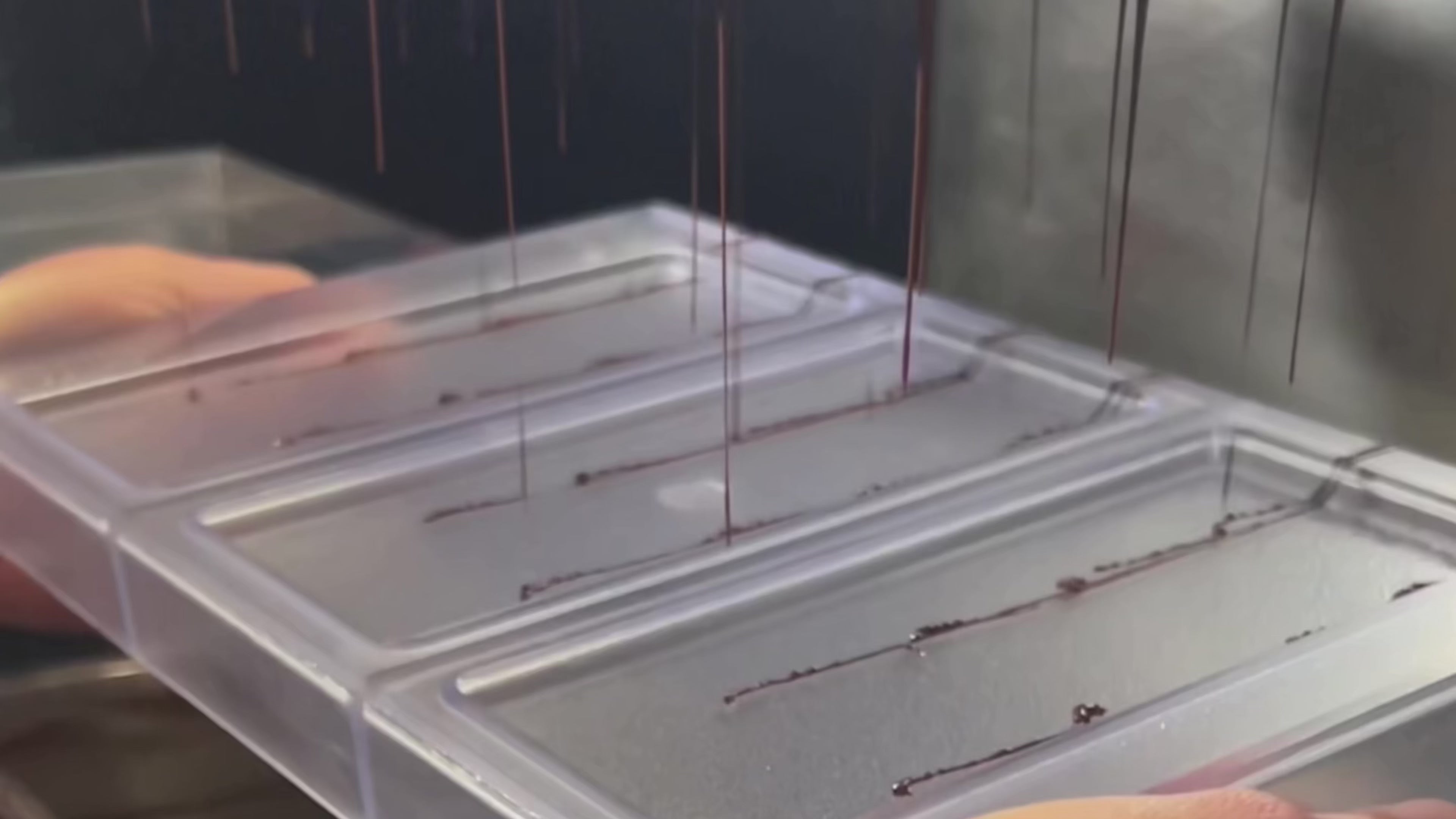 Liquid chocolate pouring from a tempering machine into a chocolate bar mold